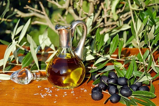 Bouteille d'huile d'olive sur une table avec des olives à côté.